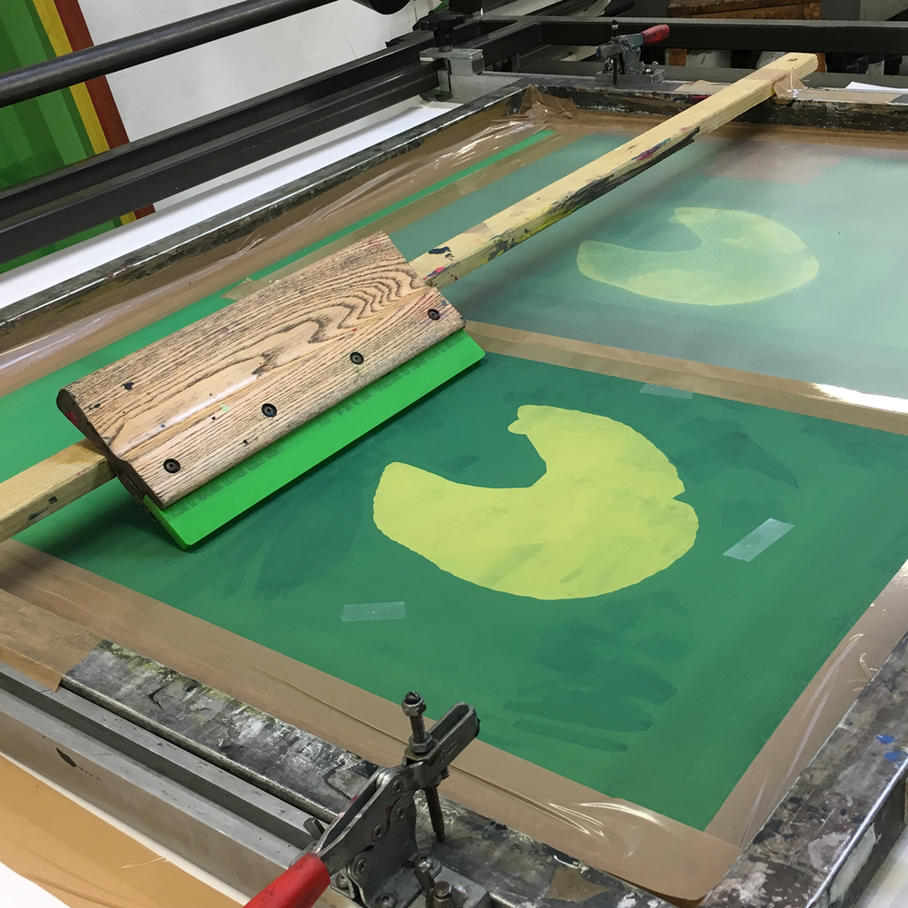 Two printing screens and a squeegee on a printing table.